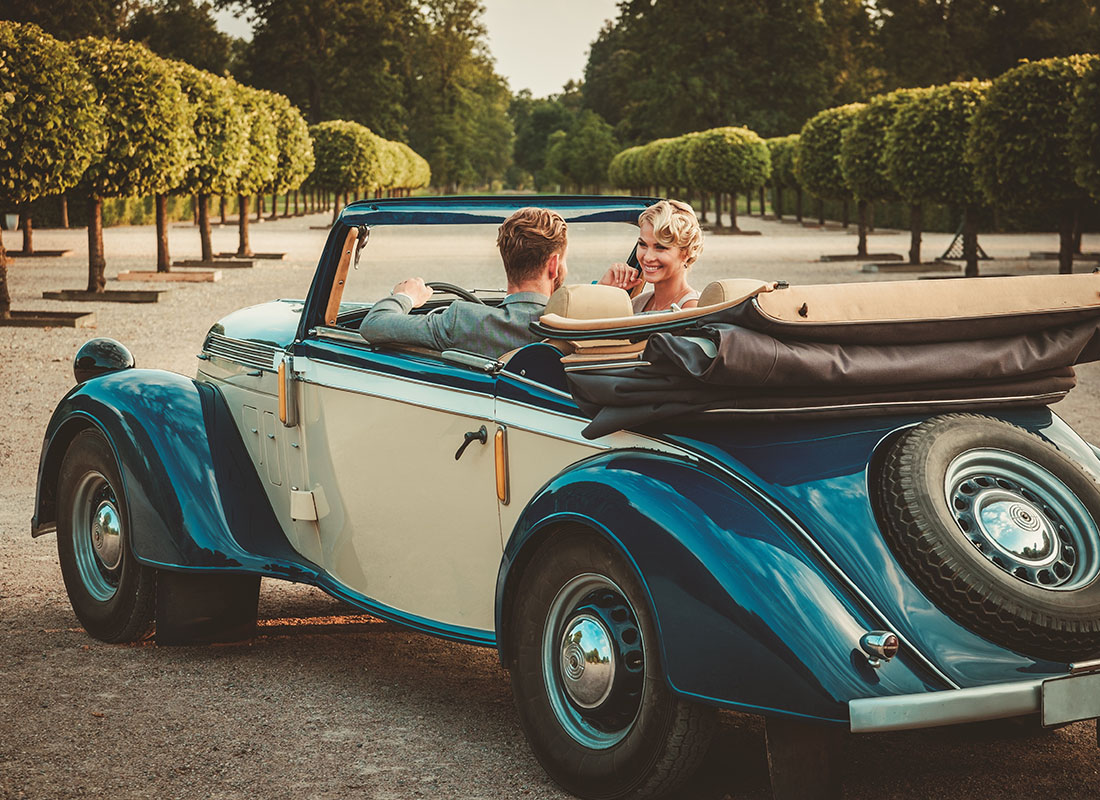 Personal Insurance - Wealthy Young Couple Sitting in their Classic Convertible on a Scenic Driveway Lined with Green Shrubs